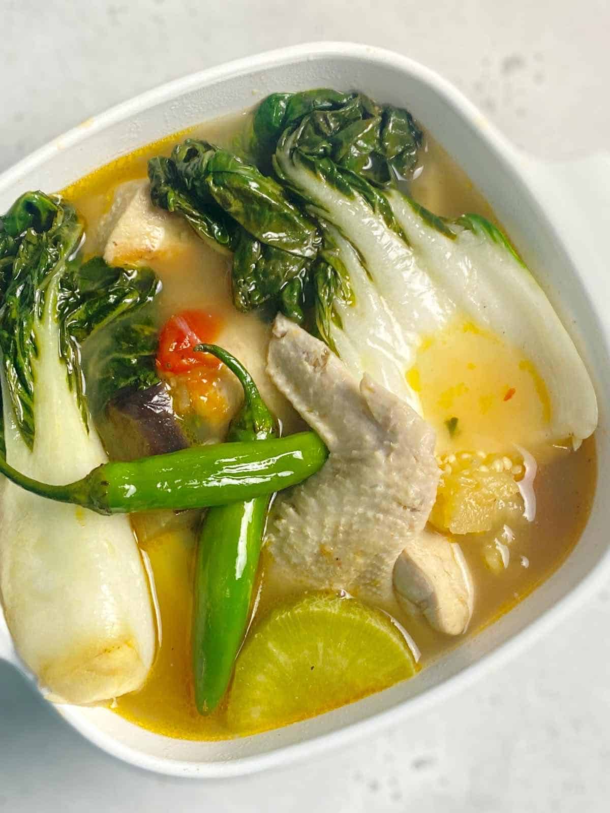 sinigang na manok topped with green chillies in a bowl bowl