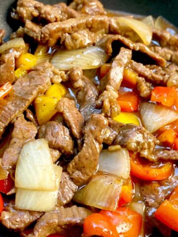 black pepper beef in a wok with red and yellow bell peppers