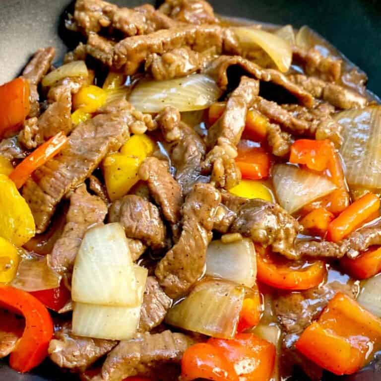 black pepper beef in a wok with red and yellow bell peppers