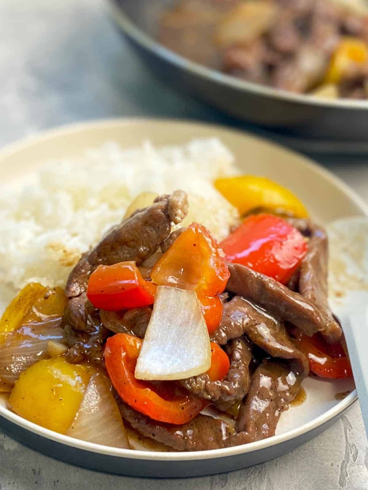black pepper beef in a serving plate with yellow and orange peppers