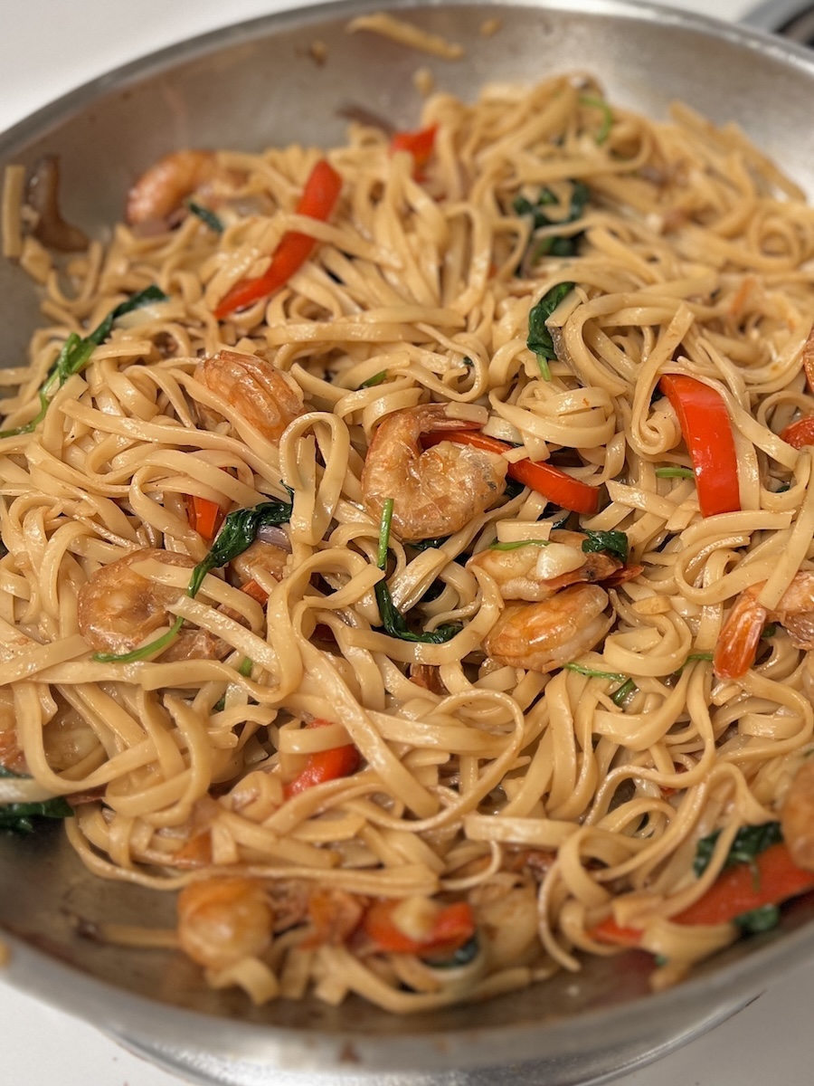 tossing cooked noodles with shrimp, spinach, and sauce in a pan