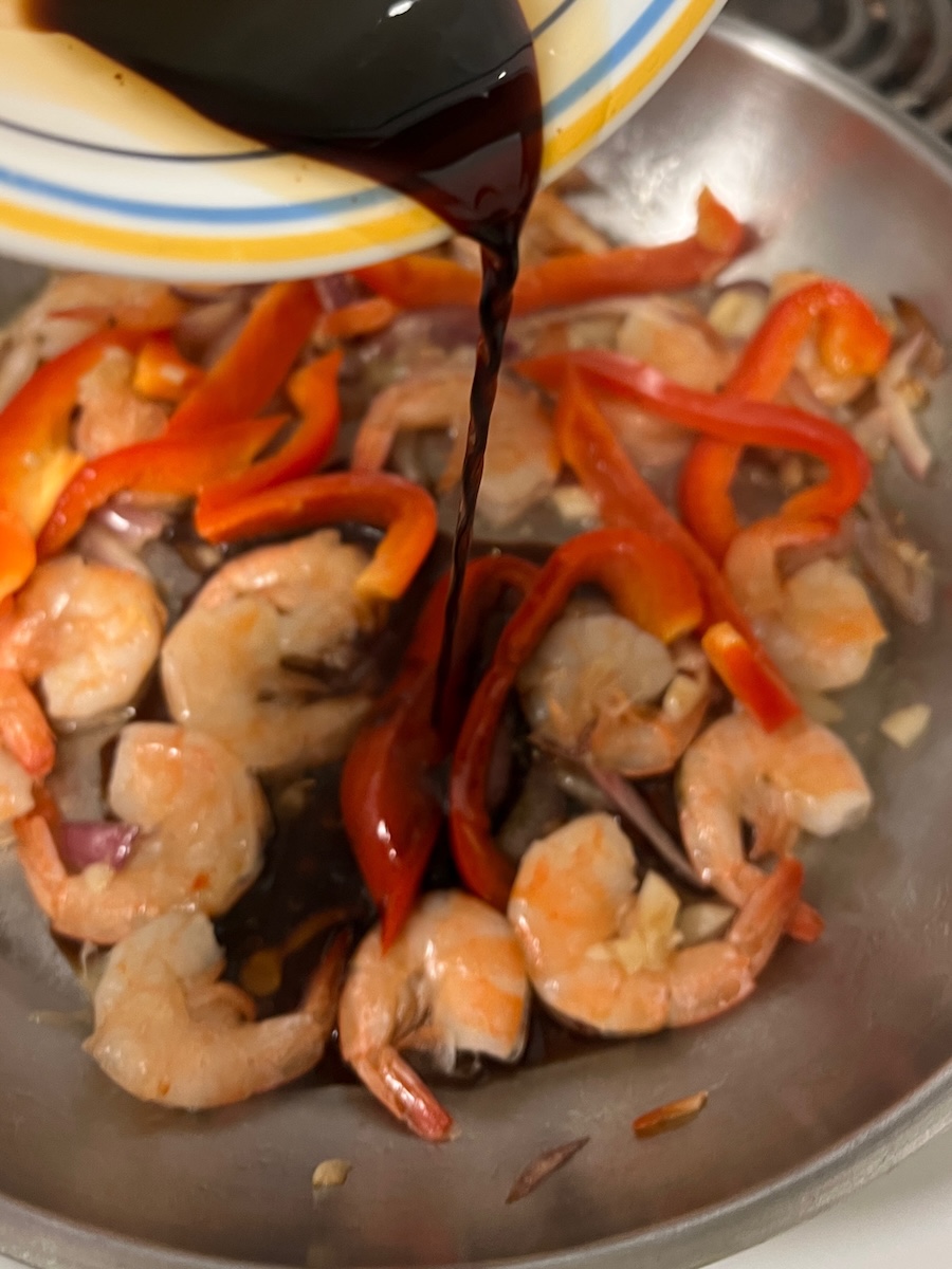 sauce being added to a pan of cooked shrimp