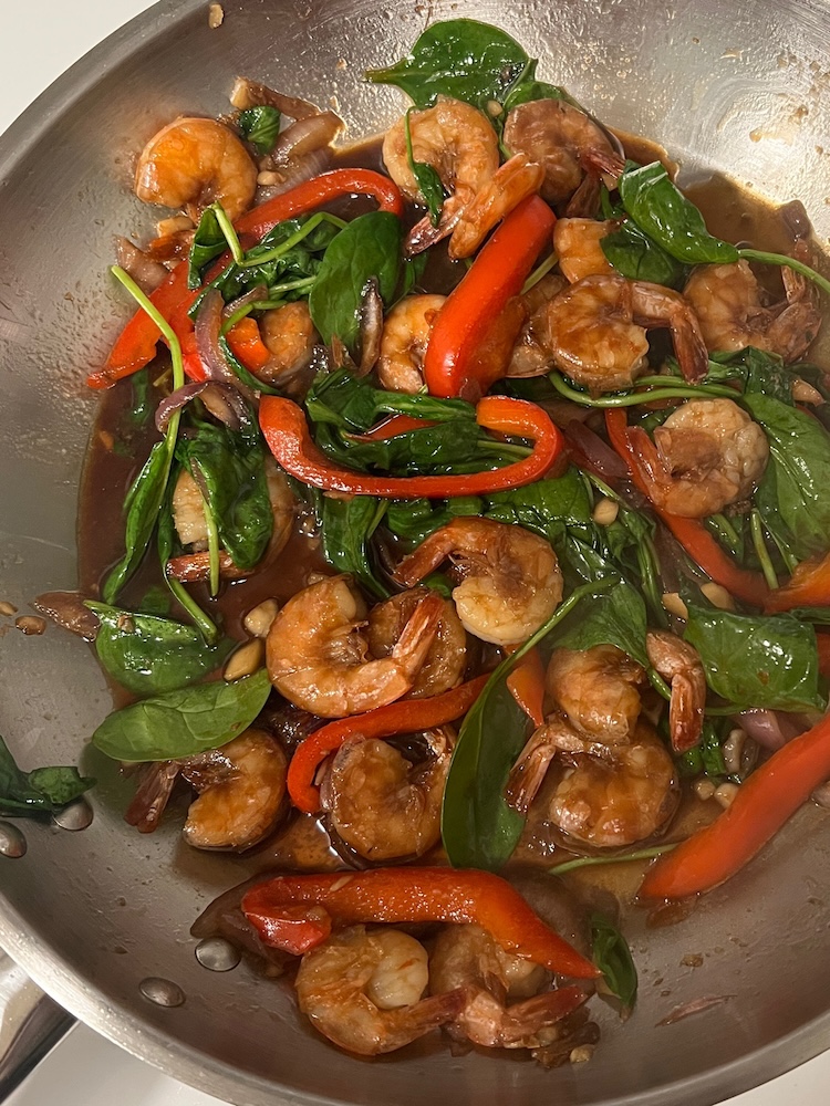 Fresh spinach added to a pan of saucy shrimp sesame noodles