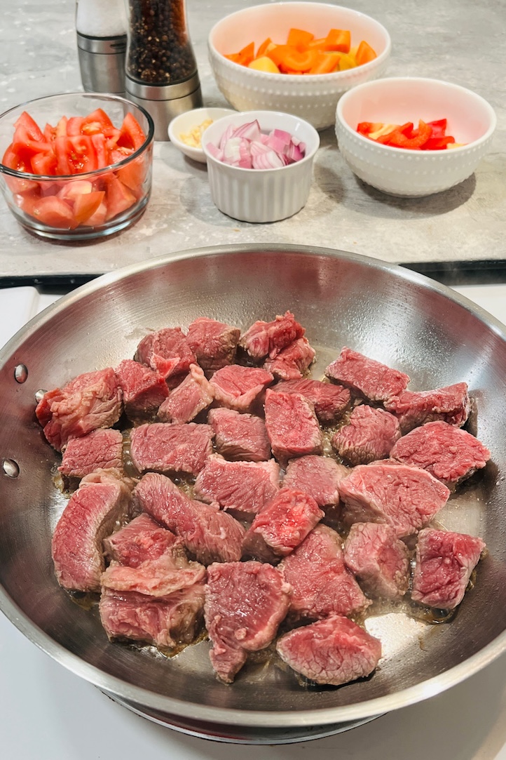 brown beef in a pan with vegetables in the background