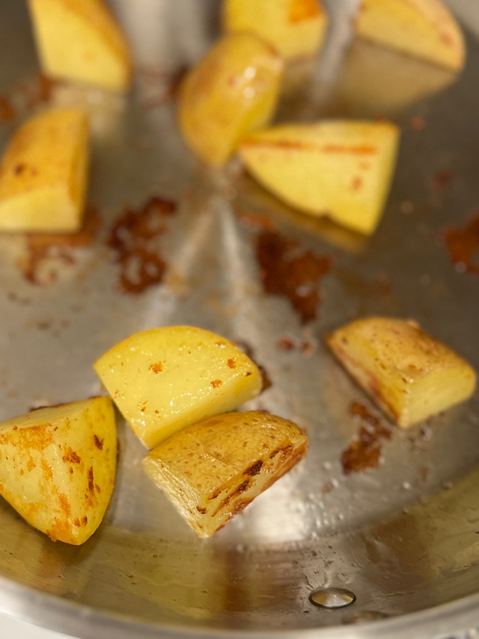 Potatoes frying in a pan until partially golden and tender.