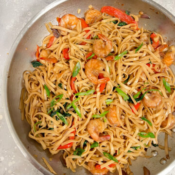 Pan of shrimp, noodles, spinach, and aromatics coated in sauce