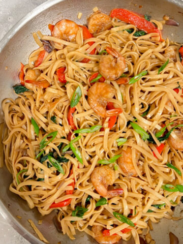 Pan of shrimp, noodles, spinach, and aromatics coated in sauce