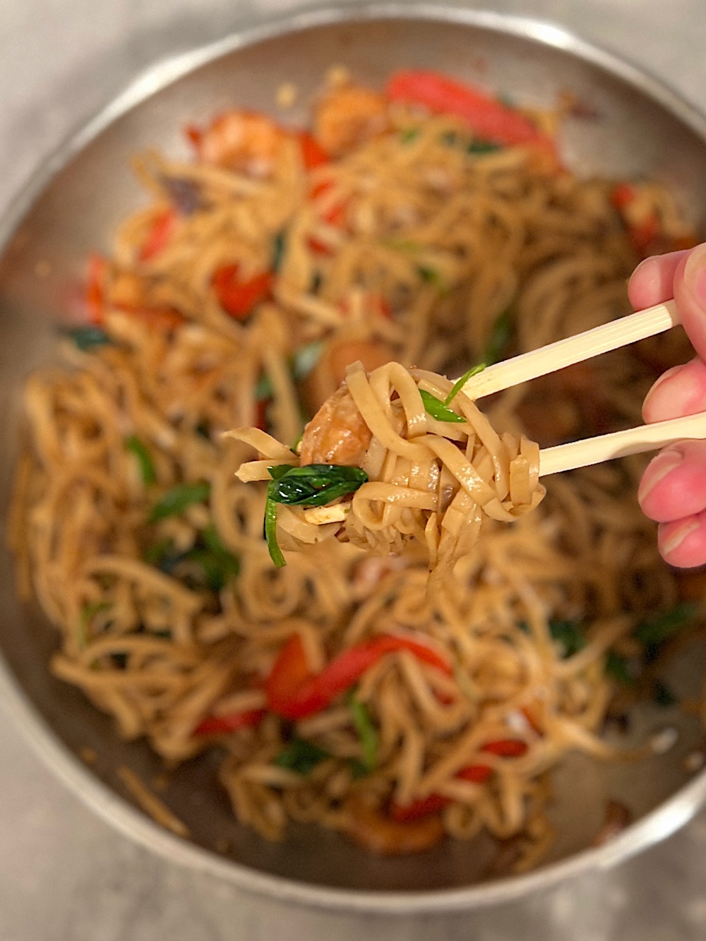 A pan filled with cooked noodles, with a pair of chopsticks lifting a portion of noodles.